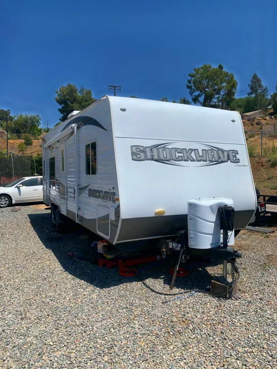 A white Forest River Shockwave travel trailer, ideal for an RV rental, is parked on a sunny gravel lot.. Forest River Other 2013