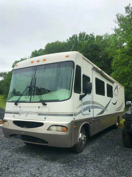 White and tan Georgetown RV, perfect for rv rental. This large motorhome is parked on gravel, set for your next travel adventure.. Forest River Georgetown 2002