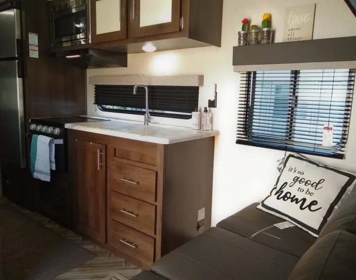 Inside a cozy RV rental: kitchen with full appliances, wooden cabinets, and a comfortable living area with decorative touches.. KZ Sportsmen 2021