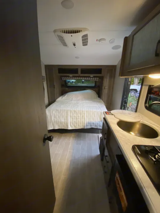 Compact RV rental interior featuring a bedroom area with a bed, a kitchen with a sink and stovetop, and an AC unit on the wall.. Sonic Lite 2021
