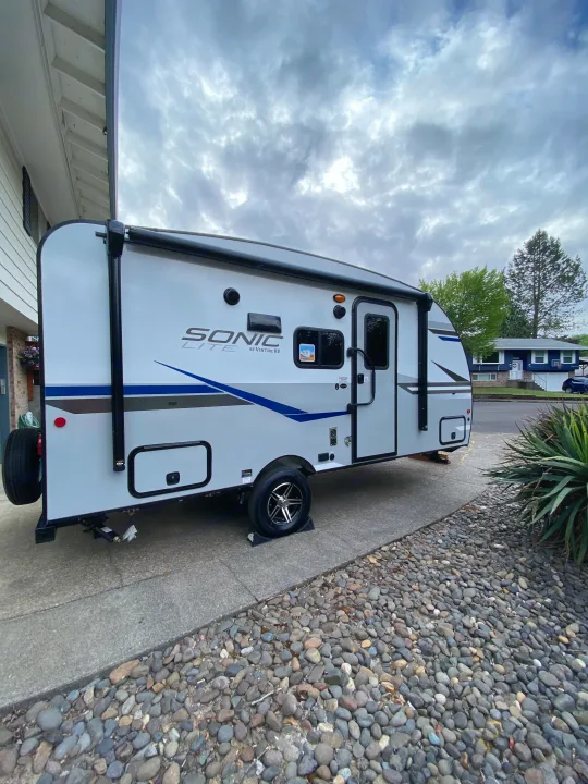 Bright white Sonic Lite travel trailer, an RV rental, parked on a residential driveway under a cloudy sky.. Sonic Lite 2021