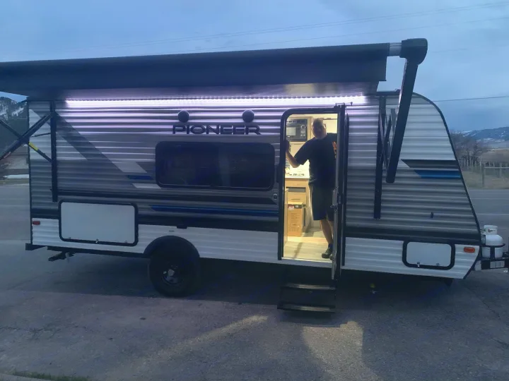 Man in the lit doorway of a modern RV with an extended awning and LED lights. Ready for your rv rental camping trip!. Pioneer BH170 2021