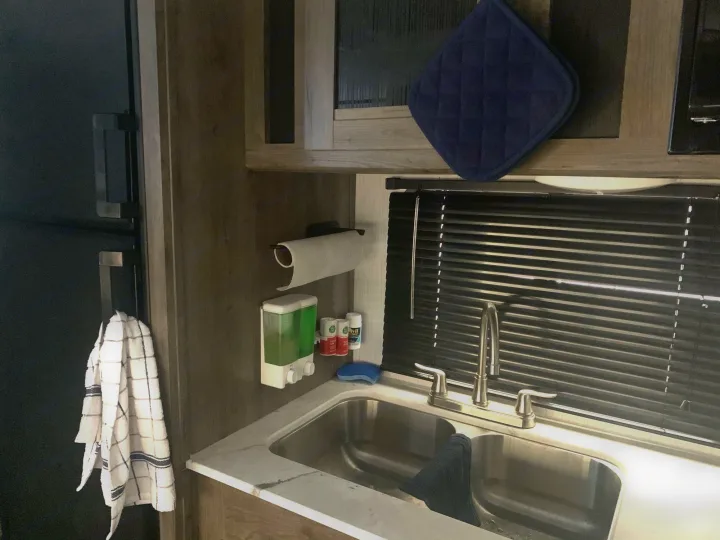 Clean RV rental kitchen features a double sink, paper towel holder, soap dispenser, and fridge with hanging towel.. Pioneer BH170 2021