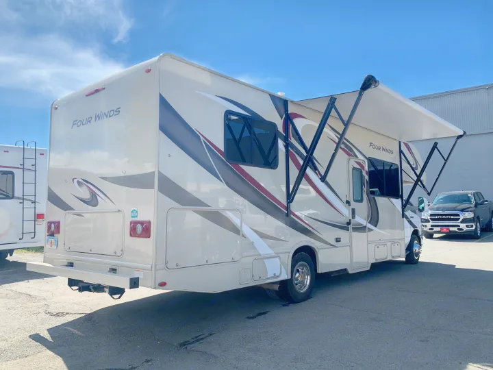 Modern "Four Winds" RV rental with an extended awning, parked outdoors on a sunny day, ready for travel adventures.. Thor Motor Coach Four Winds 2019