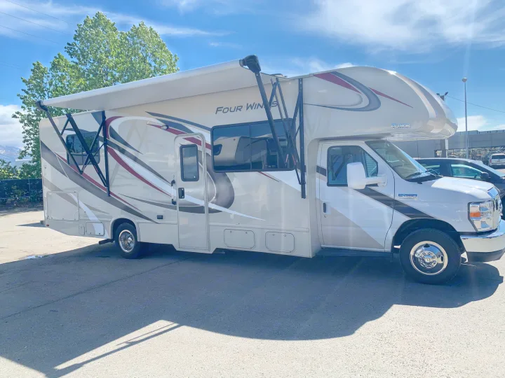 This Thor Four Winds Class C motorhome rv rental, white with graphics and an extended awning, is ready for travel.. Thor Motor Coach Four Winds 2019