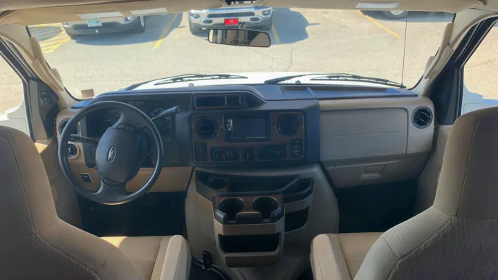 An RV rental's driver's view: spacious dashboard, Ford steering wheel, and comfortable front seats, set for adventure.. Thor Motor Coach Four Winds 2019