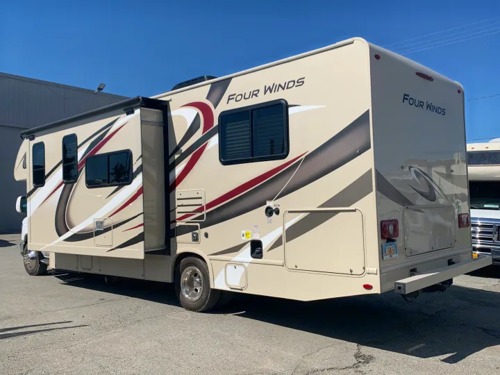 Four Winds RV rental, beige with graphic stripes, utility access visible on side. Parked outdoors.. Thor Motor Coach Four Winds 2019