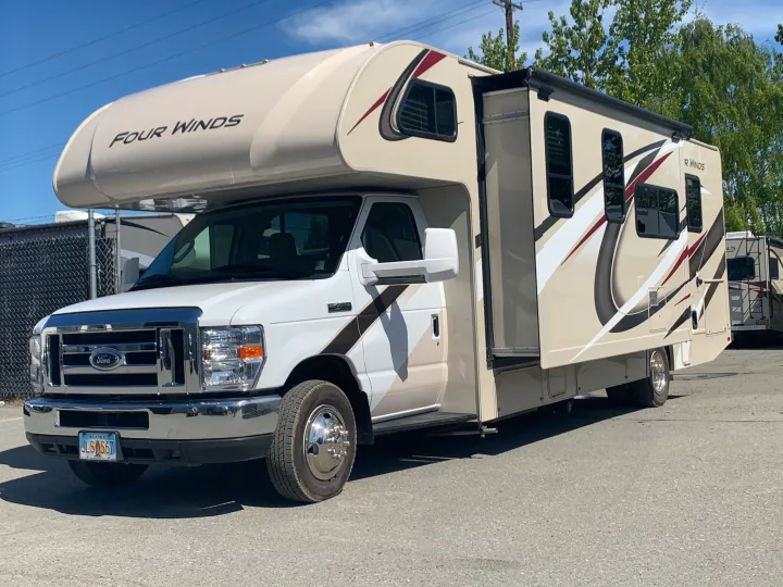 A white and tan Four Winds Class C motorhome, parked with its slide-out extended. Ideal for your next rv rental.. Thor Motor Coach Four Winds 2019