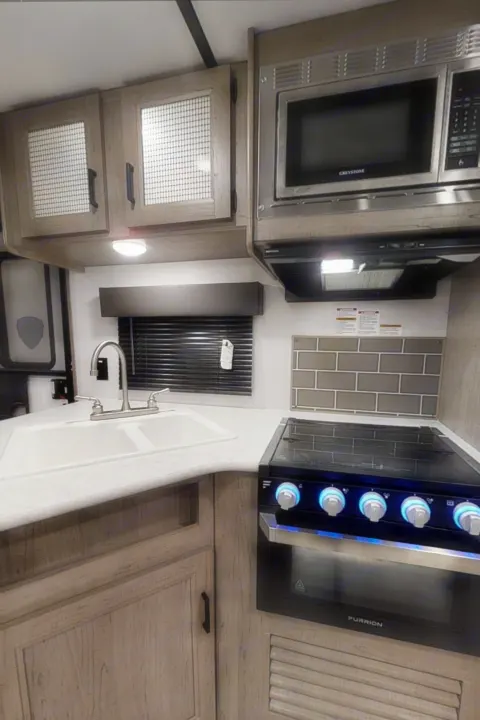 Inside an RV rental: a compact, fully-equipped kitchen with sink, microwave, oven, and wood-look cabinets.. Keystone Hideout 2021