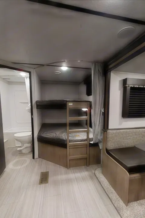 Interior view of an RV rental showing bunk beds, a small bathroom with a toilet/tub, and a cozy dining area.. Keystone Hideout 2021