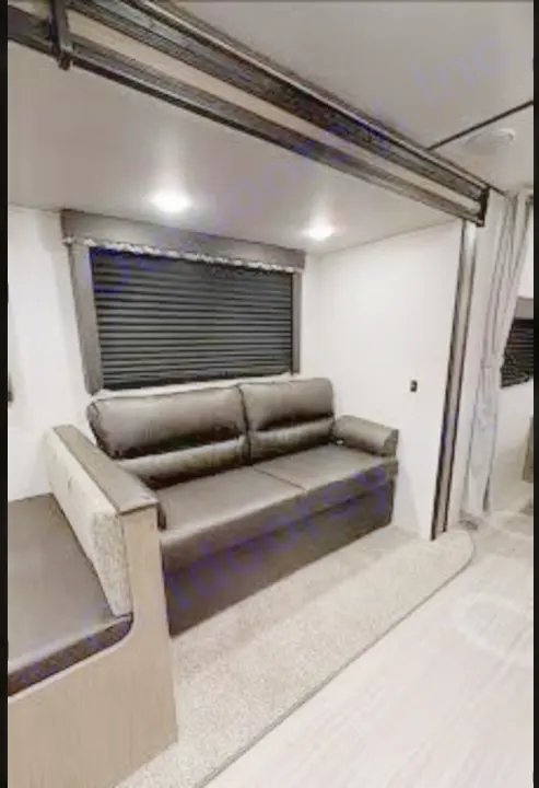 This RV rental interior shows a dark sofa, dinette, and window in a modern living space with light walls and flooring.. Keystone Hideout 2021