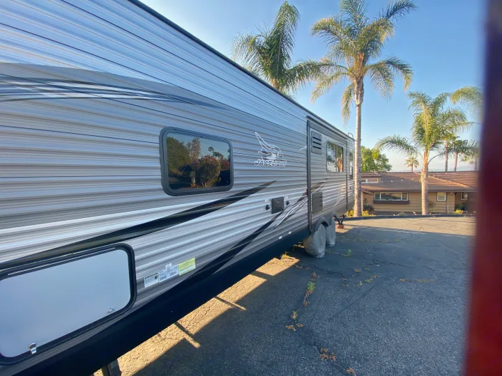 A large grey and black Jay Flight travel trailer (RV rental), parked on asphalt under palm trees.. Jayco Jay Flight 2020
