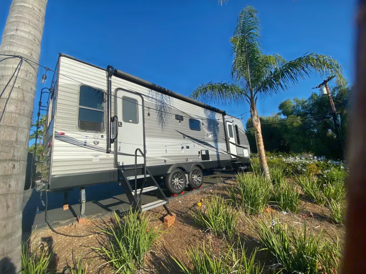 Grey travel trailer RV rental parked among palm trees with string lights, ideal for outdoor trips.. Jayco Jay Flight 2020