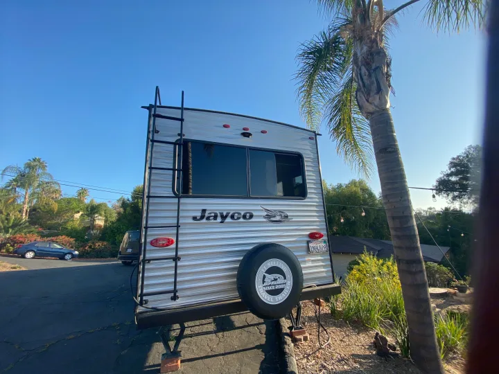 Rear view of a Jayco travel trailer with a ladder and spare tire, parked on a sunny day. A great RV rental option!. Jayco Jay Flight 2020