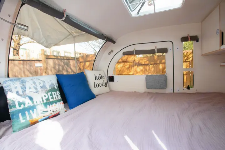 Cozy RV rental interior with a comfy bed, decorative pillows, and large scenic windows.. Droplet Teardrop 2020