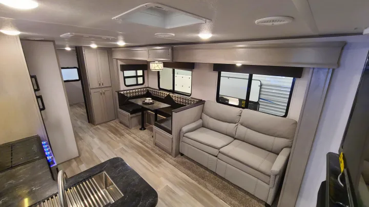 Interior of an RV rental showing a comfortable light-colored sofa, dining booth, and kitchen counter. Ideal for travel.. Forest River Tracer 2021