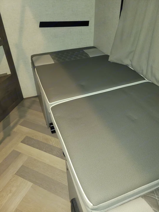 This modern gray seating area in an RV rental converts to a bed, featuring white-piped cushions and herringbone flooring.. Forest River Salem 2021