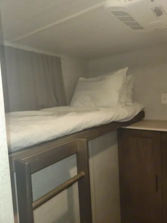 Compact RV rental bunk bed with white bedding, curtains, and overhead AC, providing cozy sleeping space.. Forest River Salem 2021