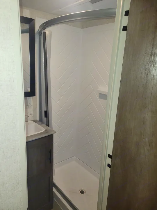 Compact RV rental bathroom with modern shower, vanity, and mirror, featuring white herringbone walls.. Forest River Salem 2021