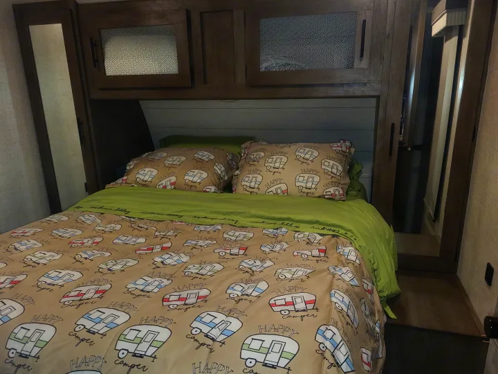 Step into comfort! This RV rental bedroom features fun 'Happy Camper' bedding and convenient overhead storage.. Forest River Salem 2021