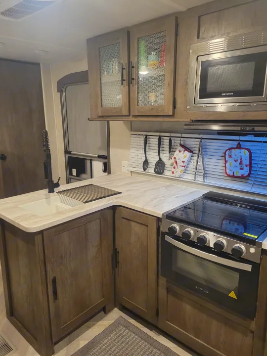 Modern RV rental kitchen with a sink, stove, microwave, wood cabinets, and cooking essentials.. Forest River Salem 2021