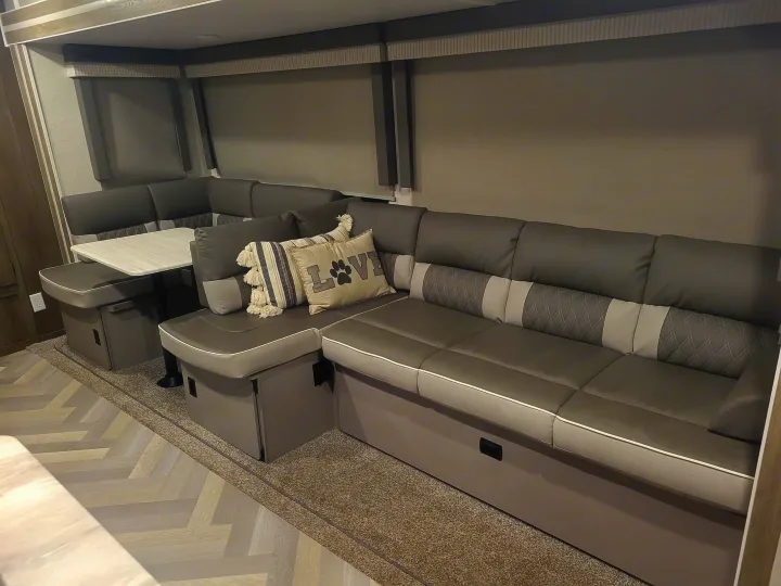 Modern grey L-shaped sofa & dinette in an RV rental interior, featuring storage and decorative pillows. Comfy travel awaits!. Forest River Salem 2021