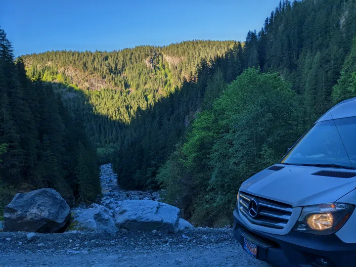 White Mercedes-Benz Sprinter RV rental on a dirt road, overlooking a forested mountain valley with a rocky riverbed.. Other Sprinter 2016