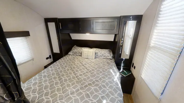 Inviting RV rental bedroom with patterned bedding, overhead storage, and bedside amenities.. Forest River Cherokee Grey Wolf 2021