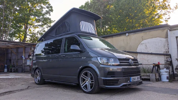 A sleek, dark grey VW pop-top camper van, perfect for RV rental adventures, with its roof raised. Parked outdoors.. vw T6 2016