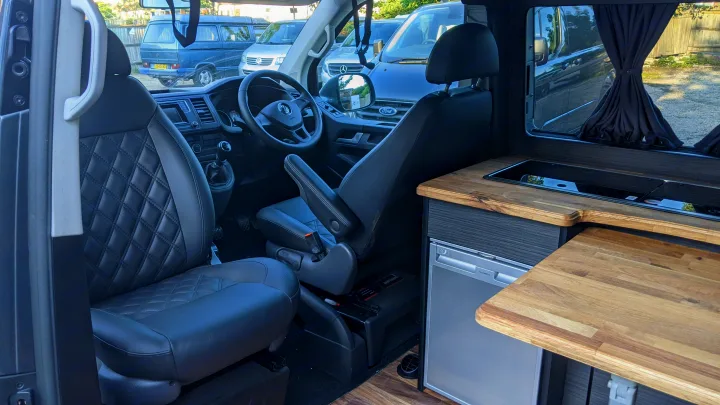 Modern RV rental campervan interior with swivel seats, dashboard, and a built-in kitchen including sink & fridge.. vw T6 2016