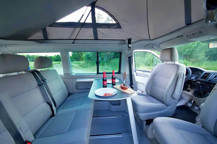 Inside an RV rental: a campervan with an extended pop-top roof, a table with two plates & drinks, and seating.. Volkswagen California Beach T6.1 2023