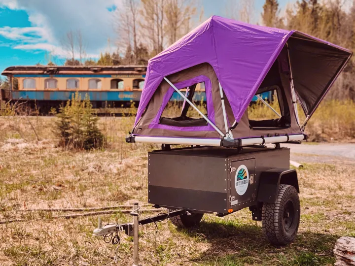 Our **rv rental** offers a compact camper trailer with a purple rooftop tent for unique outdoor adventures, pictured by an old train.. Freespirit Recreation Overland Trailer 2021