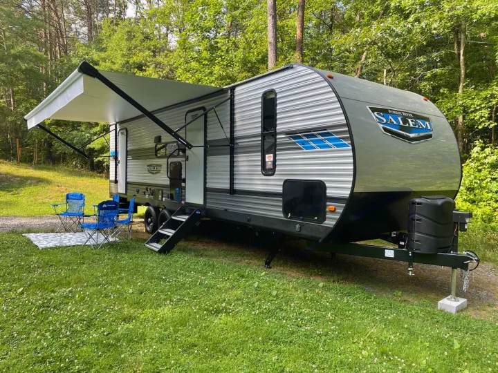 Forest River Salem RV rental with extended awning, blue chairs & mat set in a lush, wooded campsite.. Forest River Salem 2021