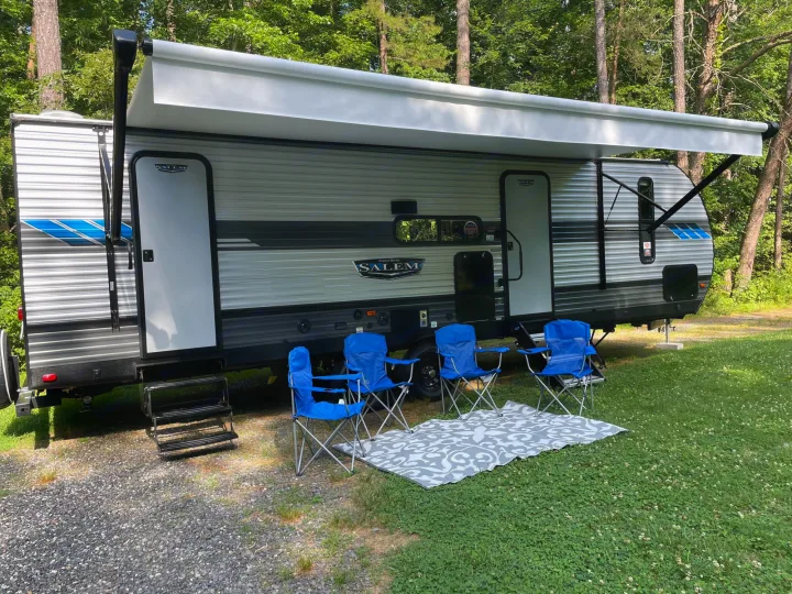 Ready for adventure! This RV rental offers an extended awning, four blue chairs, and a mat at a spacious campsite.. Forest River Salem 2021