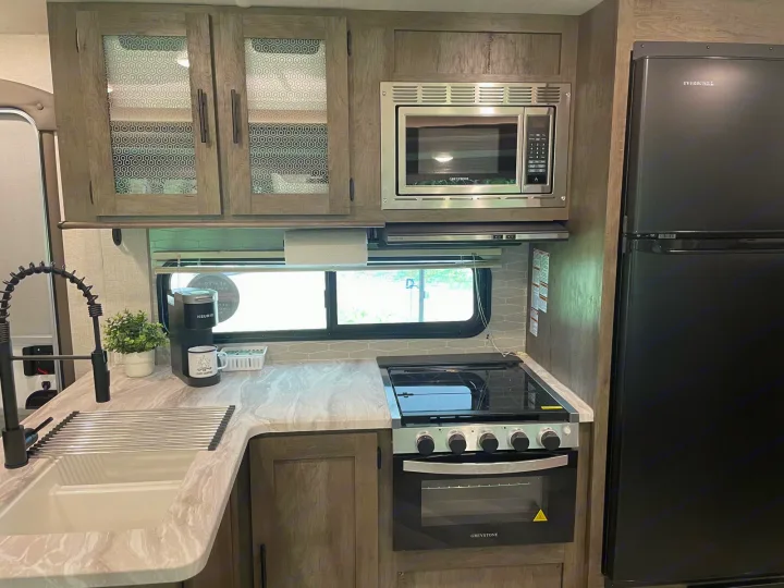Modern rv rental kitchen featuring a sleek sink, microwave, oven/stove, and refrigerator. Ideal for travelers.. Forest River Salem 2021
