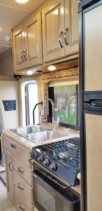 RV rental kitchen view: light wood cabinets, double sink, gas stove/oven, and fridge. Perfect for road trips!. Mercedes Benz Four Winds 2018