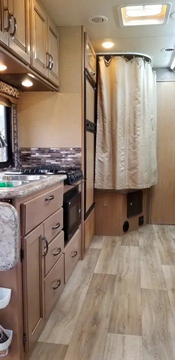 Bright RV rental interior with compact kitchen, cabinets, shower area, and wood-look flooring.. Mercedes Benz Four Winds 2018