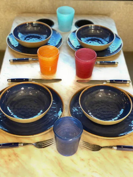 A cozy RV rental dining setup: elegant blue dishes, colorful glasses, and cutlery, perfect for meals on the go.. Winnebago Porto 2020
