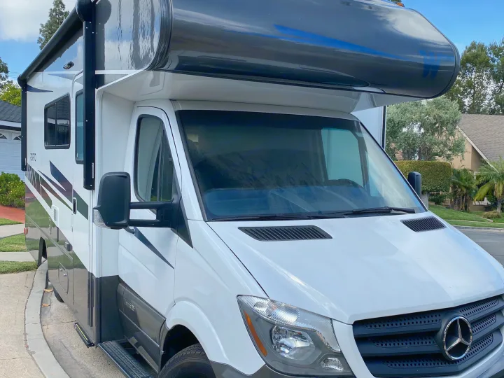 White Winnebago Porto RV rental, based on a Mercedes Sprinter chassis, parked on a street with a residential background.. Winnebago Porto 2020