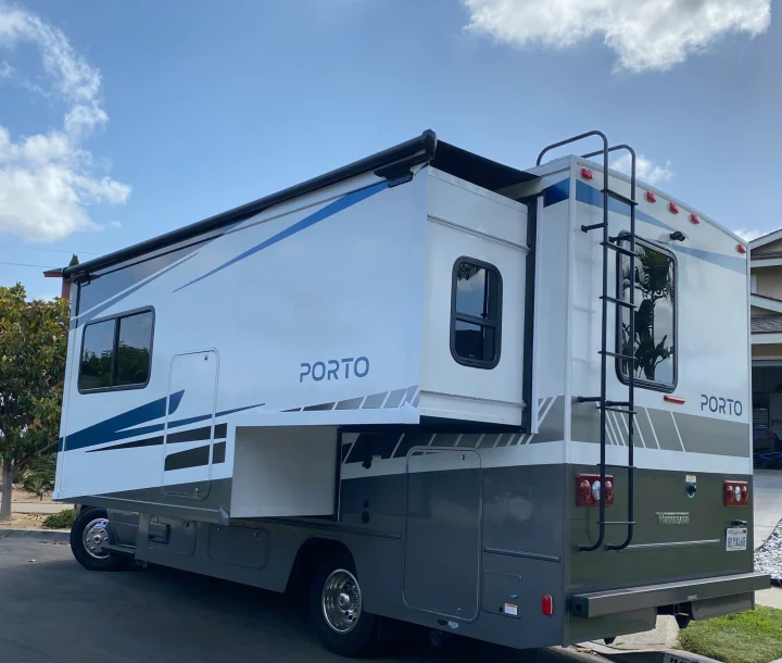 Winnebago Porto RV rental, a white and gray motorhome with an extended slide-out and rear ladder.. Winnebago Porto 2020