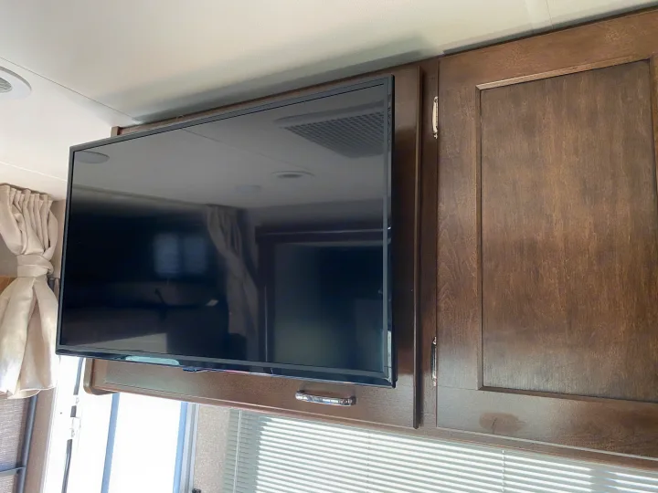 RV rental interior: A flat-screen TV is mounted below overhead wooden cabinets, above windows with horizontal blinds.. Winnebago Porto 2020