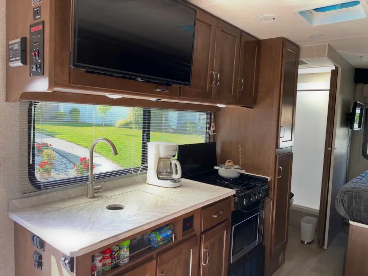 Inside a modern RV rental, a kitchen area with sink, stove, microwave, coffee maker, and wall-mounted TV for your trips.. Winnebago Porto 2020