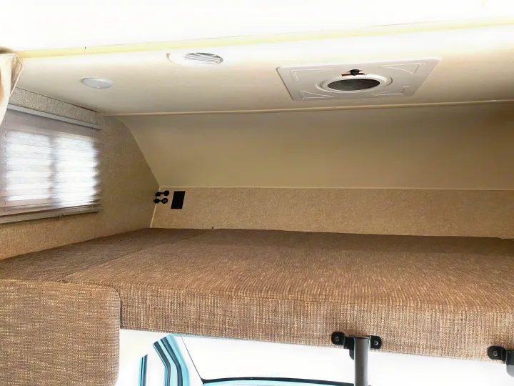 Experience comfortable sleeping in this RV rental's cab-over bunk, featuring a cozy mattress, window blinds, and ceiling lights.. Winnebago Porto 2020