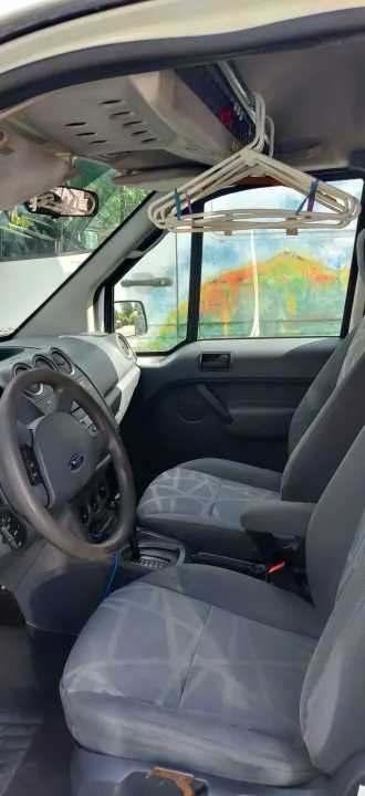 Inside an rv rental van: grey patterned seats, Ford steering wheel, and hangers. Scenic mural visible through the windshield.. Ford Connect 2012
