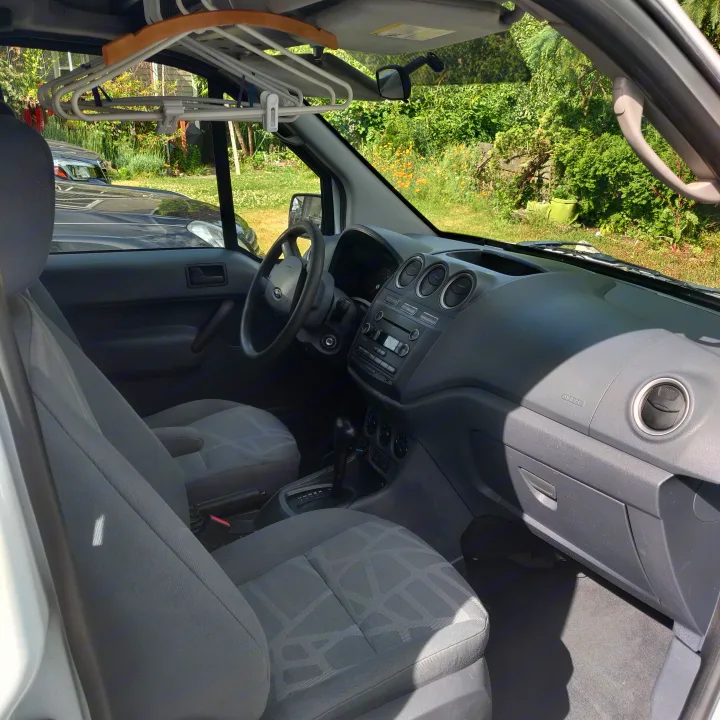 RV rental van interior: dashboard, steering wheel, and front seats. Hangers in cabin suggest travel readiness.. Ford Connect 2012