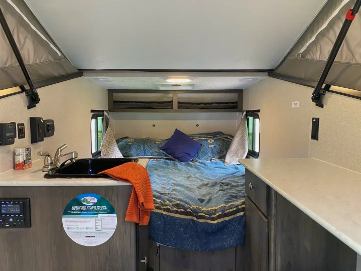 Step inside this compact RV rental, featuring a cozy bed, kitchen sink, and counter. Perfect for camping and road trips!. Coachmen Clipper 2021
