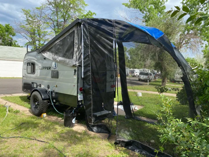 A gray Clipper travel trailer, perfect for your next rv rental, features an attached screen room at a serene campsite.. Coachmen Clipper 2021