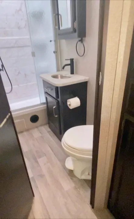 Compact RV rental bathroom featuring a white toilet, black vanity with sink, and a shower with frosted glass.. Jayco Alante 2021