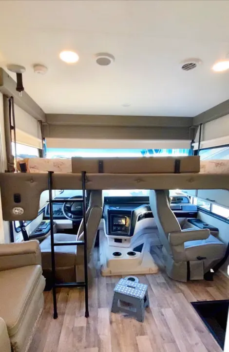 Spacious RV rental interior featuring a cozy bunk bed above the cockpit, accessible by a ladder, for comfortable travel.. Jayco Alante 2021