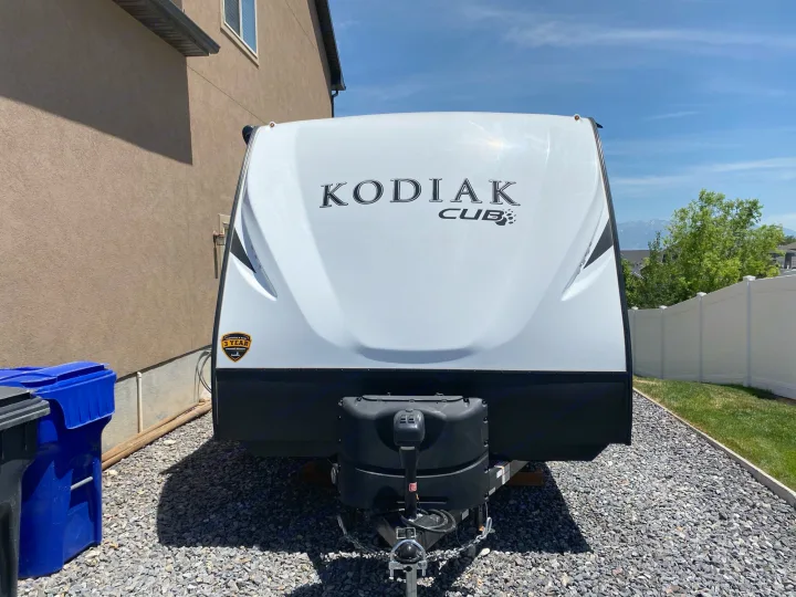 Front view of a white Kodiak Cub travel trailer, ready for RV rental adventures. It's parked on gravel next to a house.. Dutchmen Kodiak 2021